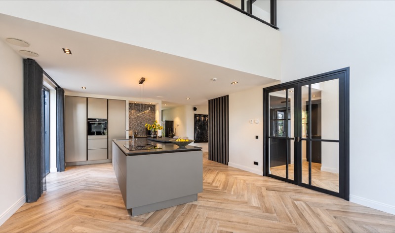 Licht interieur met hoge wanden, keukeneiland en donkere glazen deuren
